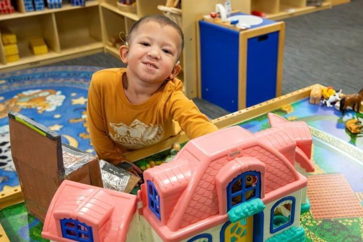 Young boy with hearing aids playing with toys in a classroom.